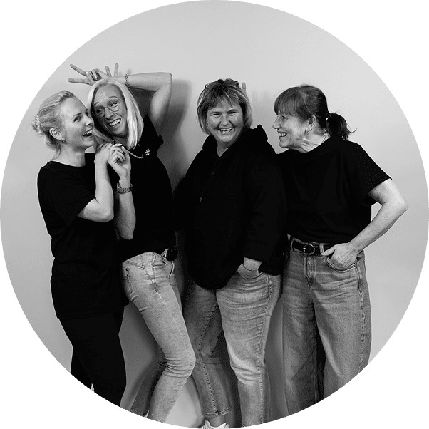 Vier Frauen in schwarzen Oberteilen posieren fröhlich – sympathisches Teamfoto im Bereich Über uns.