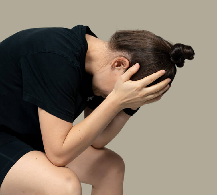 Frau mit depressiver Körperhaltung hält sich verzweifelt den Kopf – Symbolbild für psychische Belastung, die durch gezielte Physiotherapie unterstützt werden kann.