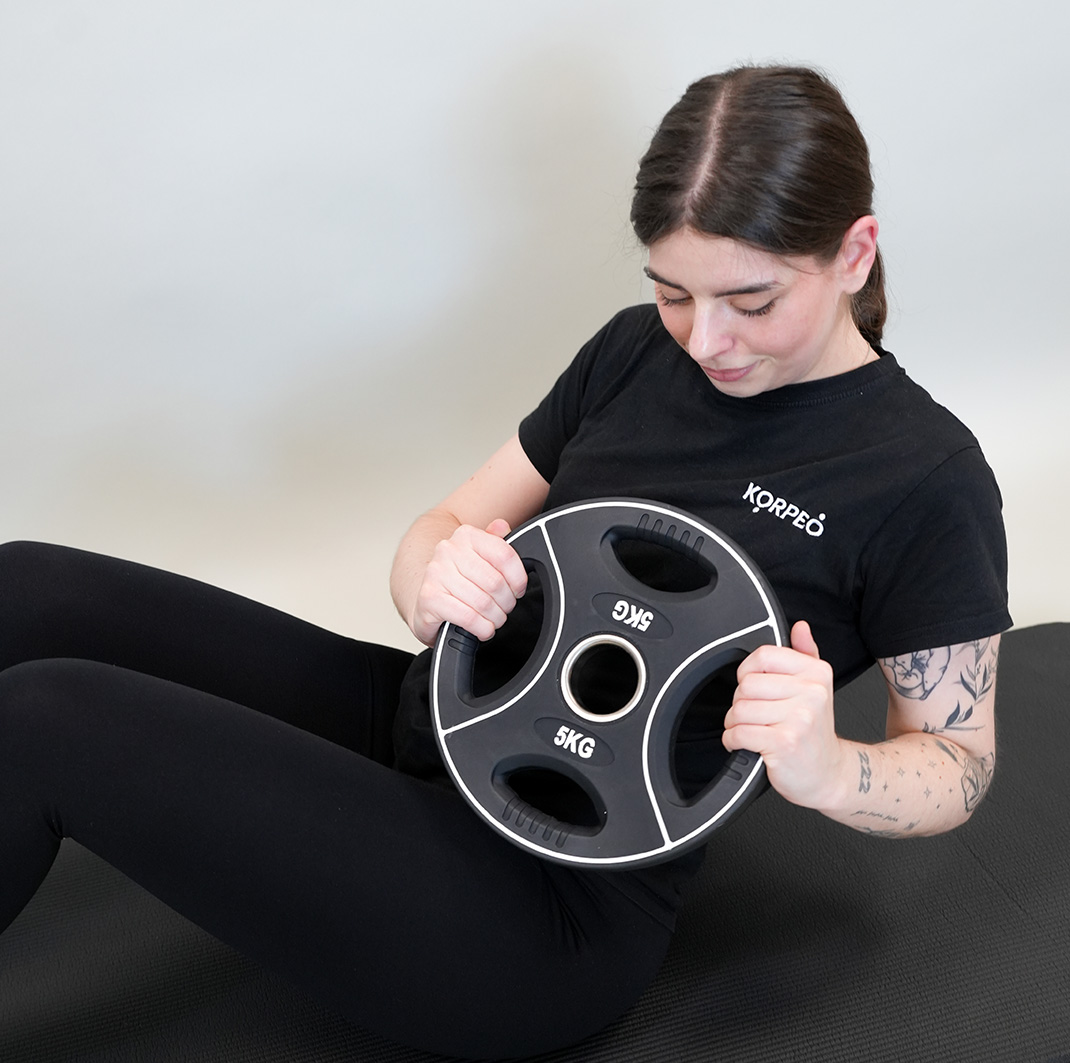 Junge Frau trainiert auf einer schwarzen Matte ihren Bauch mit einer Hantelscheibe