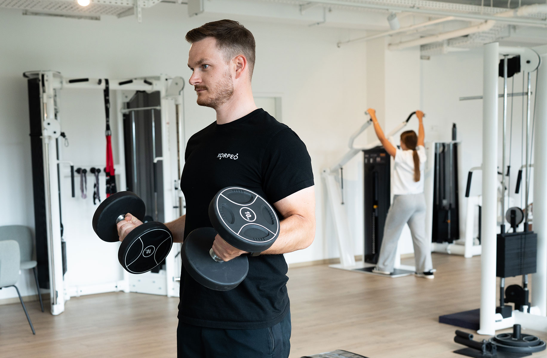 Junger Mann trainiert auf der Trainingsfläche mit zwei Hanteln.
