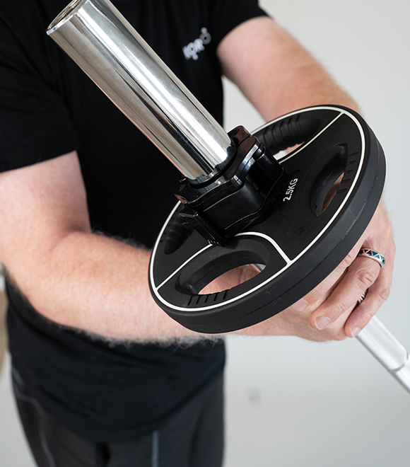 Trainer Marcus hält eine Langhantel in der Hand und führt eine Übung durch